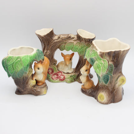 A ceramic hornsea pottery woodland animal centerpiece featuring a tree trunk base with three tree-stump holders, green leafy sides, and small painted squirrel and deer figurines in the center on a light gray background.