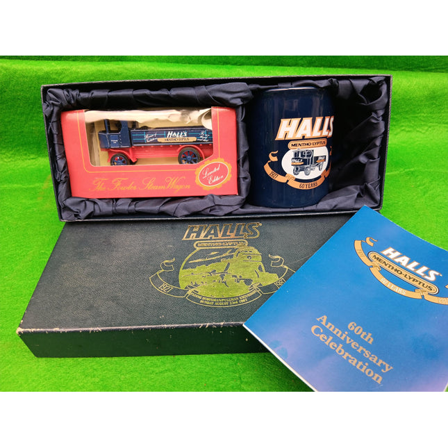A boxed Halls Midland Railway 60th Anniversary gift set on a bright green background. The set includes a miniature model train lorry in a clear window box, a dark blue ceramic mug with Halls branding, a black presentation box with gold crest, and a blue booklet.