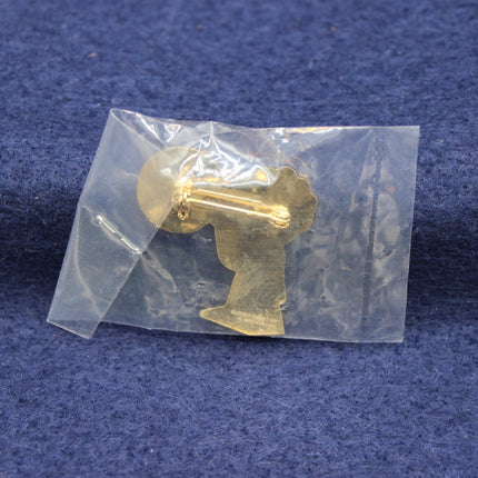 Gold-colored Golly Badge in a clear plastic bag on a blue background
