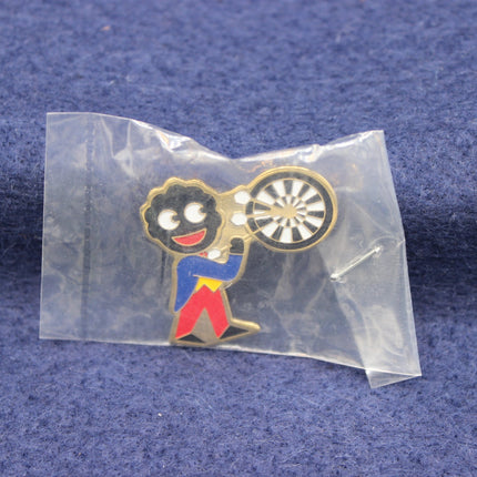Pin with a golliwog character holding a dartboard in clear packaging on a blue fabric background