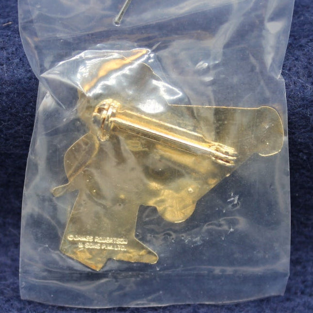 Gold-colored metal Golly badge in a clear plastic bag on a blue fabric background