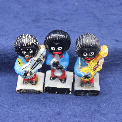Three small  Golly figurines with golliwog heads on a blue background