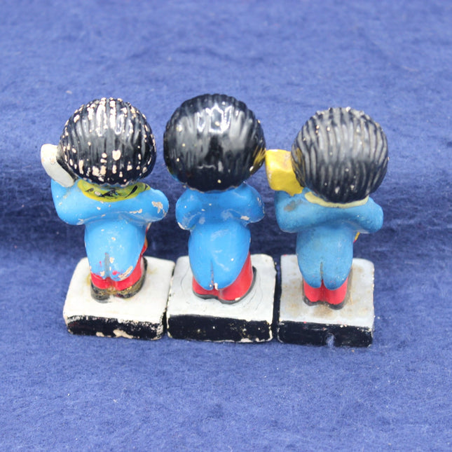 Three small blue characters with black hats sitting on a white block against a blue background