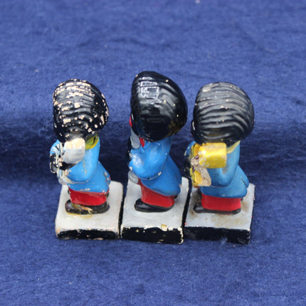 Three small Golly figurines with blue outfits and black hats on a blue background