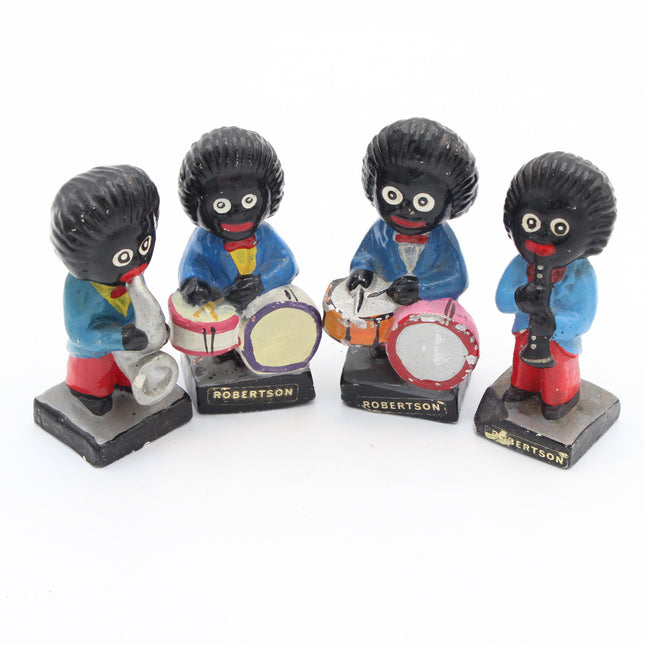 Four small painted figurines of Gollies dressed as a band, with black hair, blue jackets, and red pants, playing silver trumpet, drums, and tambourine. Each figure stands on a black base labeled ROBERTSON.