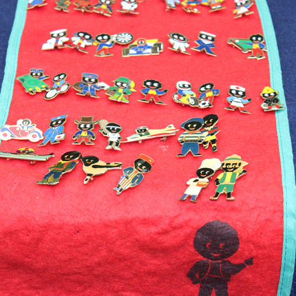 A collection of colorful enamel lapel pins shaped like Robertson's Golly characters, displayed on a red fabric mat with a turquoise border.