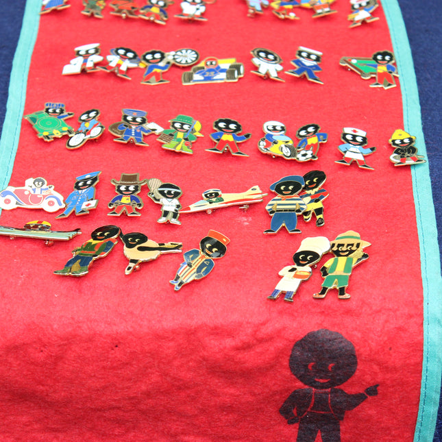 A collection of colorful enamel lapel pins shaped like Robertson's Golly characters, displayed on a red fabric mat with a turquoise border.