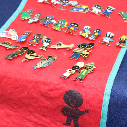 A collection of colorful Robertson's Golly enamel pins featuring stylized cartoon characters, displayed on a red fabric runner with a turquoise border.