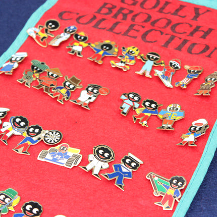 A close-up of a red display scroll labeled 'GOLLY BROOCH COLLECTION' with multiple colorful enamel Golly brooch pins featuring stylized figures, photographed on a blue surface.