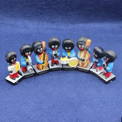 Set of eight small Golly figurines with black hair, colorful clothing, and musical instruments on a blue background.
