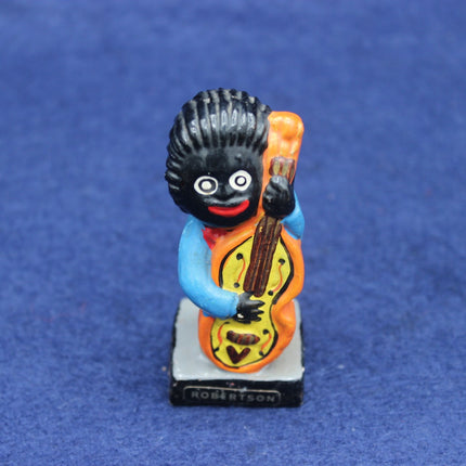 Figurine of a Golly character with a black face, blue outfit, and orange guitar on a blue background