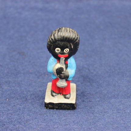 Small figurine of a Golly character with a black hairstyle, red outfit, and holding a microphone on a blue background.