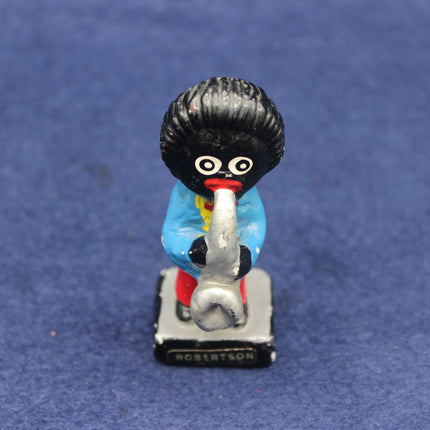 Small figurine of a Golly character with a black bob, blue shirt, and red shoes on a blue background
