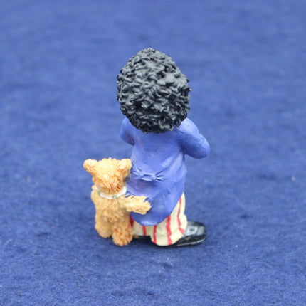 Small figurine of a Golly with curly hair holding a teddy bear on a blue background