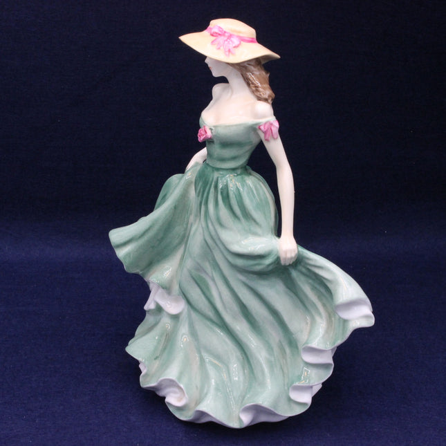 Porcelain figurine of a woman in a green dress and straw hat on a dark blue background