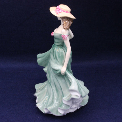 Porcelain figurine of a woman in a green dress and pink hat on a dark blue background