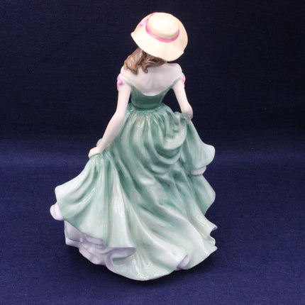 Porcelain figurine of a woman in a green dress and straw hat on a dark blue background