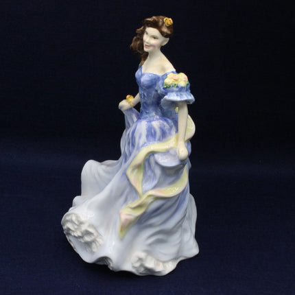 Porcelain figurine of a woman in a blue dress holding flowers on a dark background