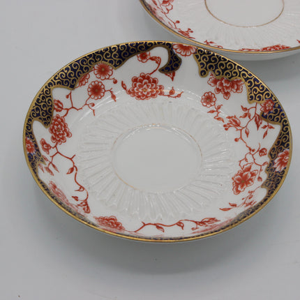 A white porcelain plate with a red floral pattern and a navy blue and gold border, shown on a light gray background with another plate partially visible in the top right.