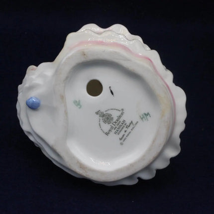 The underside of a white porcelain shell-shaped object, showing a printed Royal Mint London 1935 mark and a small blue bead detail, set against a dark navy background.