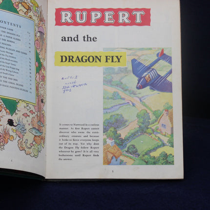 Open book with 'Rupert and the Dragon Fly' illustration on a dark background