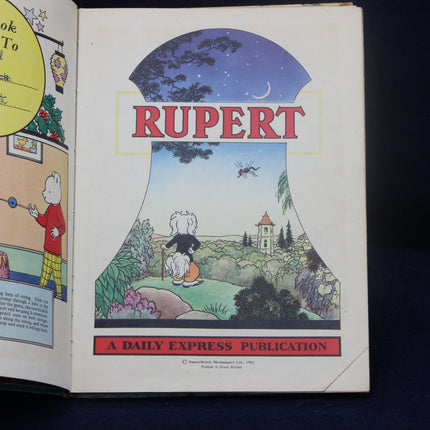 Open book showing a Rupert Bear illustration with 'Rupert' and 'Daily Express Publication' text.