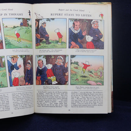 Open book with illustrated pages featuring Rupert Bear and other characters on a dark background