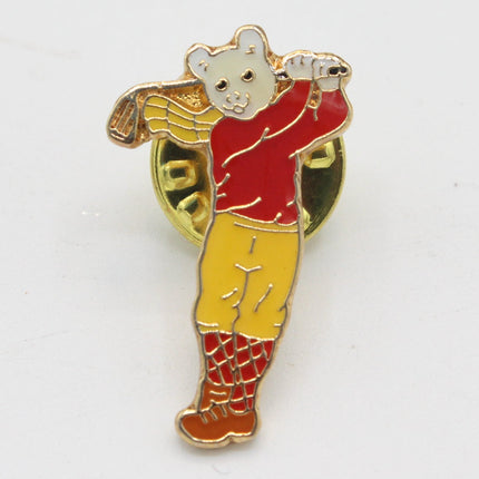 A small enamel pin shaped like a bear wearing a red sweater and yellow pants, holding a baseball bat, photographed on a plain white background.