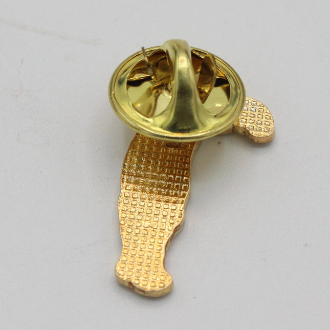 A gold-colored enamel pin showing its back side with the clasp mechanism, placed on a plain light gray background.