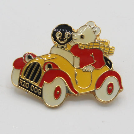 A small enamel pin depicting a white mouse wearing a red shirt and gold scarf, driving a yellow and red vintage car with black wheels and grille, on a plain white background.