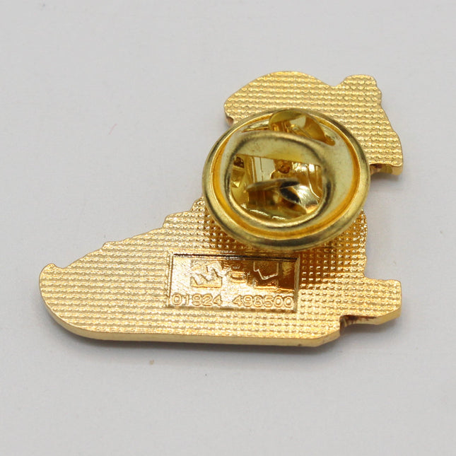 A small gold-colored metal pin or badge with a textured surface and a circular clasp, photographed on a plain light gray background.