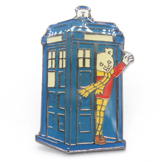 A small enamel pin shaped like a blue TARDIS police box, with a cartoon character peeking out from the door and waving. The pin is photographed on a clean white background.