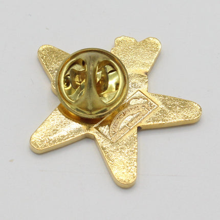 A small gold-colored enamel pin shaped like a five-pointed star, showing the metal clutch backing on one side, photographed on a plain light gray background.
