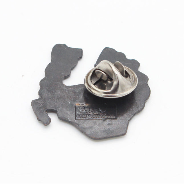 The back of a small metal pin or badge with an irregular dark gray silhouette shape and a silver spring clasp, photographed on a plain white background.