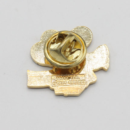 A small gold-colored metal pin or badge with a heart-shaped outline and a central circular clasp, photographed on a plain light gray background.