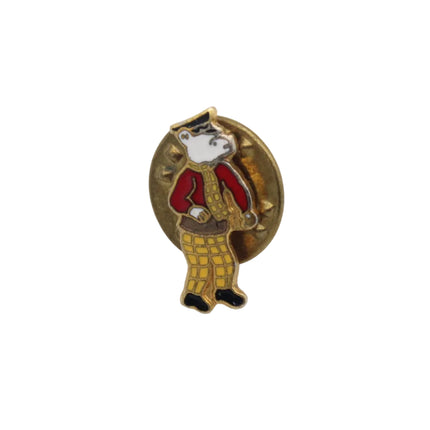 A small enamel pin featuring a stylized Rupert bear wearing a red jacket, yellow plaid pants, and a black-and-white face, mounted on a gold-tone oval backing, shown on a plain white background.