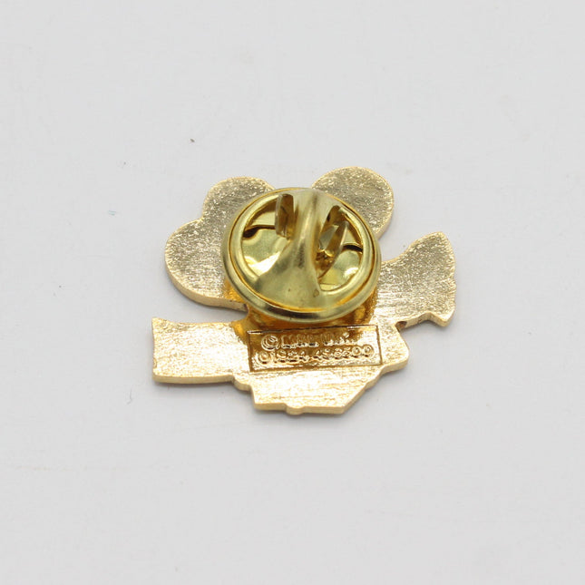 Gold-colored metal lapel pin showing the back side with a heart-shaped pin backing and a small rectangular charm, photographed on a plain light gray background.