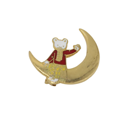 A small enamel pin featuring rupert bear wearing a red jacket, riding a gold crescent moon on a plain light background.