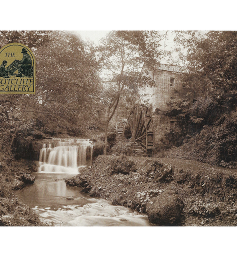 Black and white photograph of a watermill with a waterfall and surrounding trees.