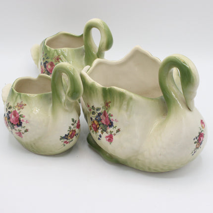 Three ceramic swan-shaped creamers with floral rose patterns in pink, red, and green, arranged on a white background.