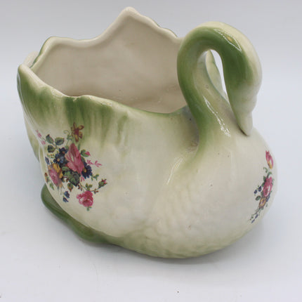 A vintage ceramic swan-shaped pitcher with a green handle and base, featuring a floral print on the sides, set against a plain white background.
