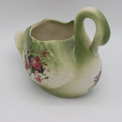 A vintage ceramic planter shaped like a swan, featuring a glossy green and cream glaze with a floral pattern on the side, set against a plain light gray background.