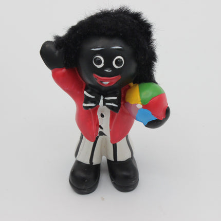 A small black vinyl figurine of a Golly character with a black afro, wearing a red jacket, white shirt, and black bow tie, holding a multicolor beach ball.