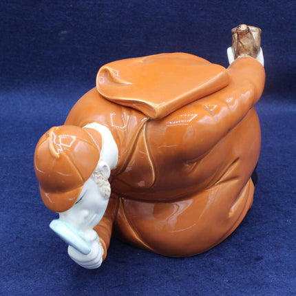 Brown ceramic sculpture of a figure with a hat on a blue background