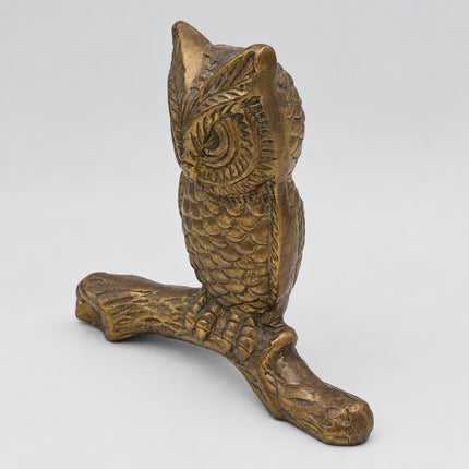 A vintage-style metallic gold owl figurine perched on a branch, photographed against a seamless light gray background.