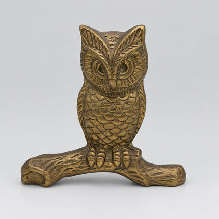 A vintage-style metallic owl figurine perched on a branch, finished in a warm gold/brass tone, photographed against a neutral light gray background.