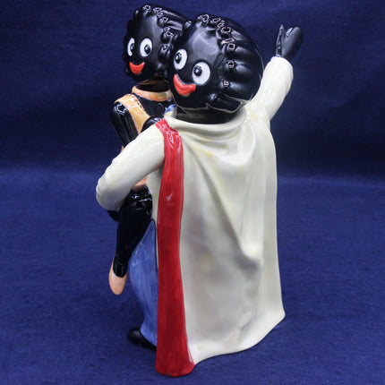 Figurine with a black figure on its back, wearing a white garment and red scarf against a blue background