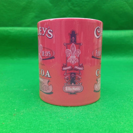 A pink ceramic coffee mug with vintage-style printed logos and text, standing upright on a bright green background.
