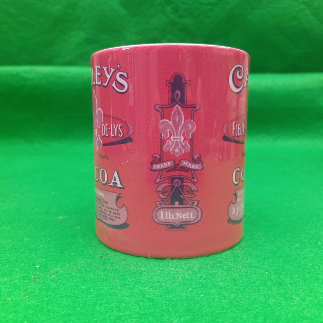 A pink ceramic coffee mug with vintage-style printed logos and text, standing upright on a bright green background.