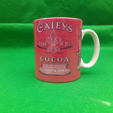 A vintage-style ceramic mug featuring the Caley's Cocoa logo, with a coral-pink body and a white handle, set against a bright green background.